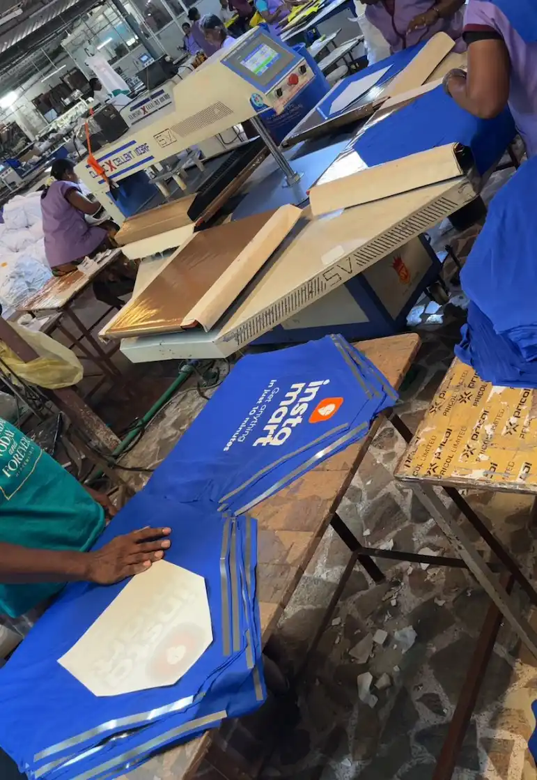 Industrial heat press machine printing custom client logo on corporate blue uniforms and promotional t-shirts