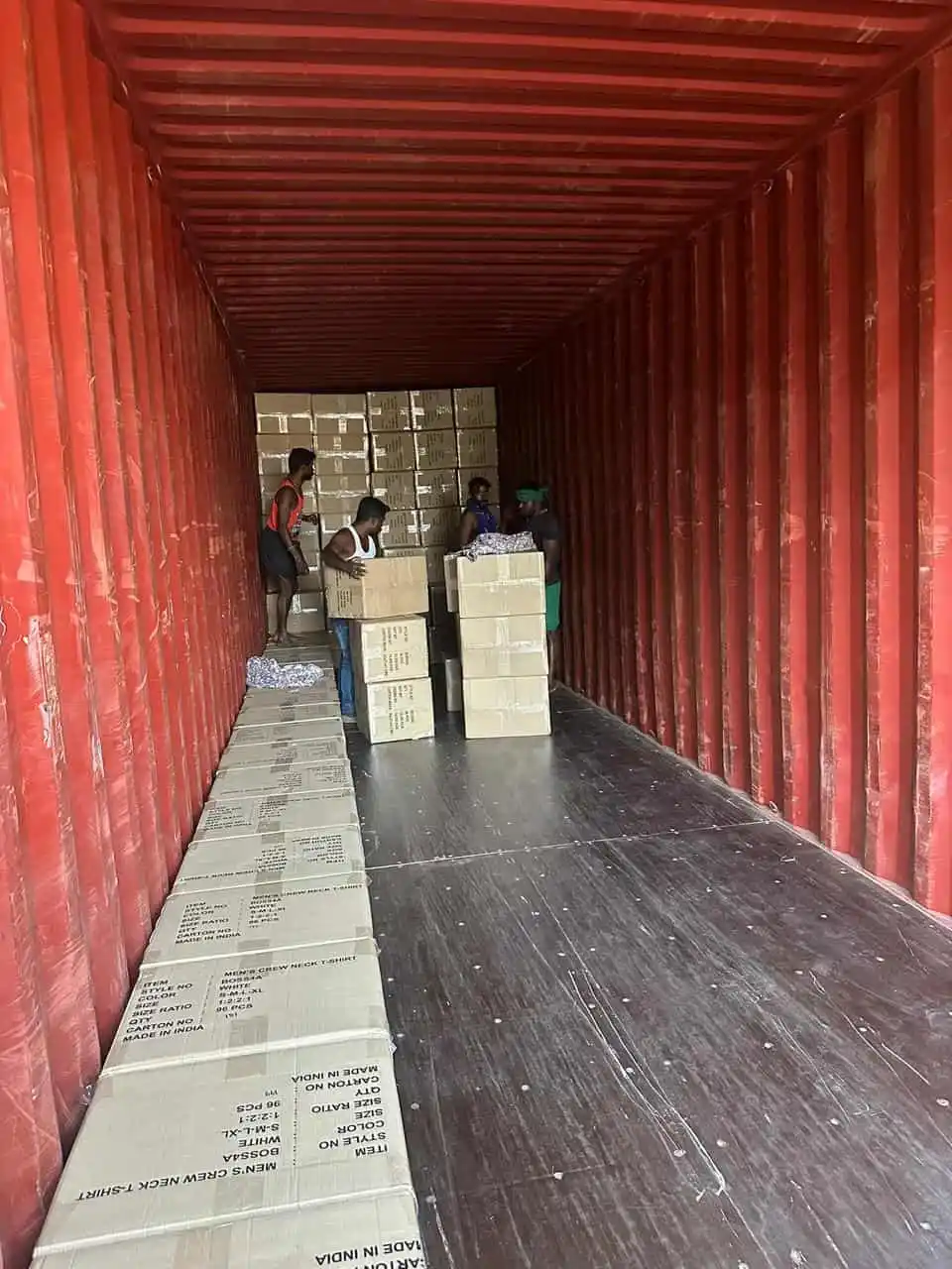 Logistics team loading packed corporate t-shirt cartons inside a large freight container